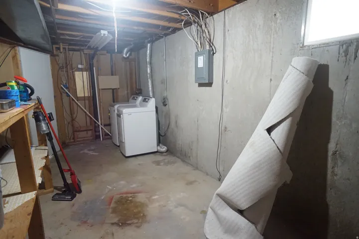 Unfinished basement with concrete walls, exposed ceiling joists, and a utility window