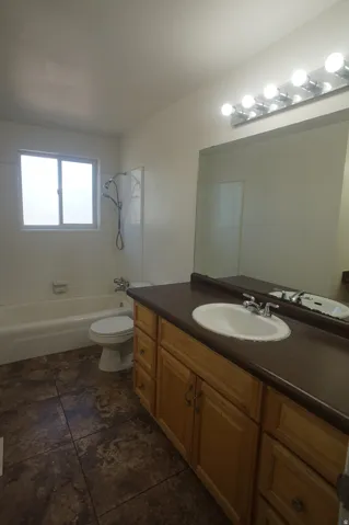 Spacious master bathroom featuring dual vanities with wood cabinetry, dark countertops, and an illuminated mirror