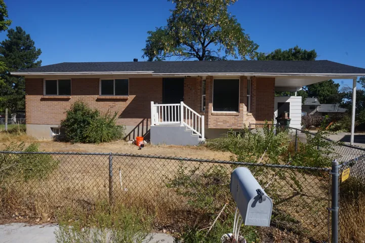 Brick exterior with a dark shingle roof, white front porch railing, and a covered carport