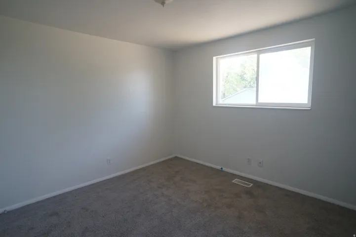 Window with white frame, gray carpeted flooring, white walls, and white ceiling
