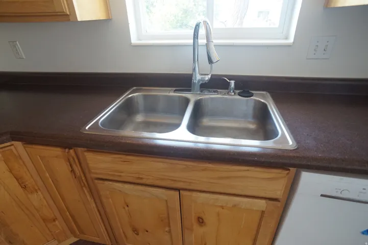 Stainless steel double basin sink with a chrome faucet, set into a dark countertop