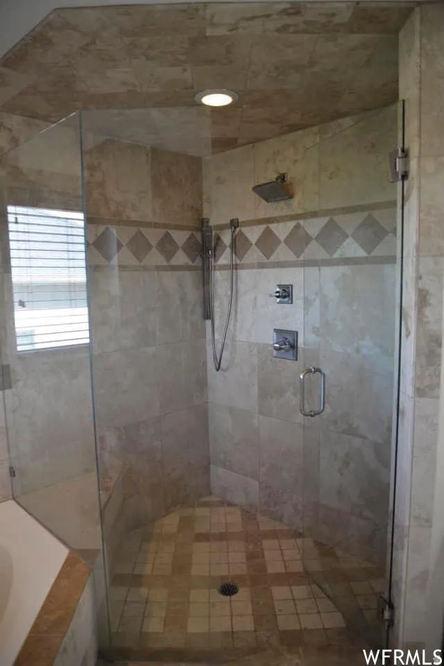 Tiled shower enclosure with a glass door, wall-mounted showerhead, handheld shower fixture, and recessed lighting