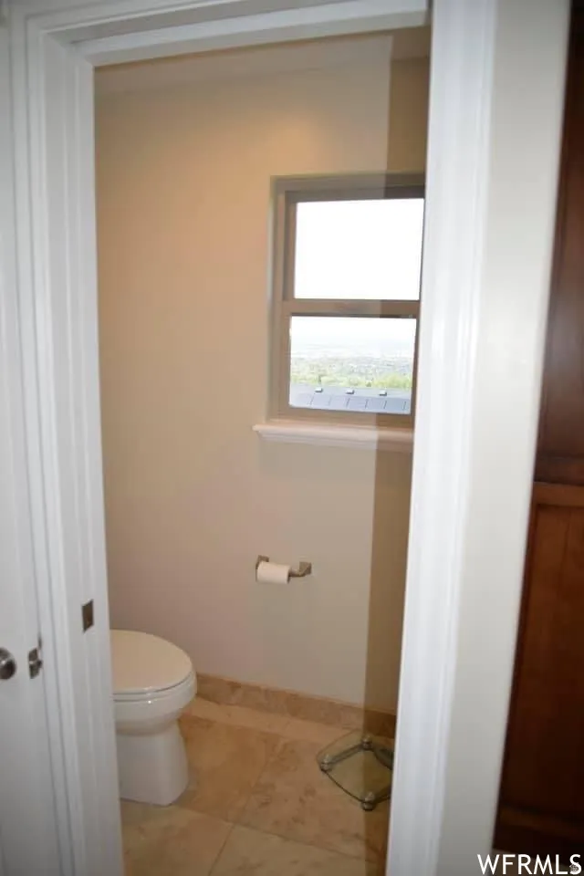 Wall-mounted lighting, single window, tiled flooring, and a built-in toilet