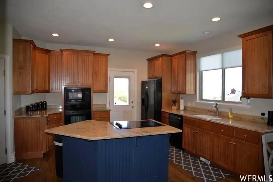 Kitchen featuring wood-finish cabinetry, light-toned countertops, a central island with a built-in cooktop, recessed lighting, and a window with roller shades
