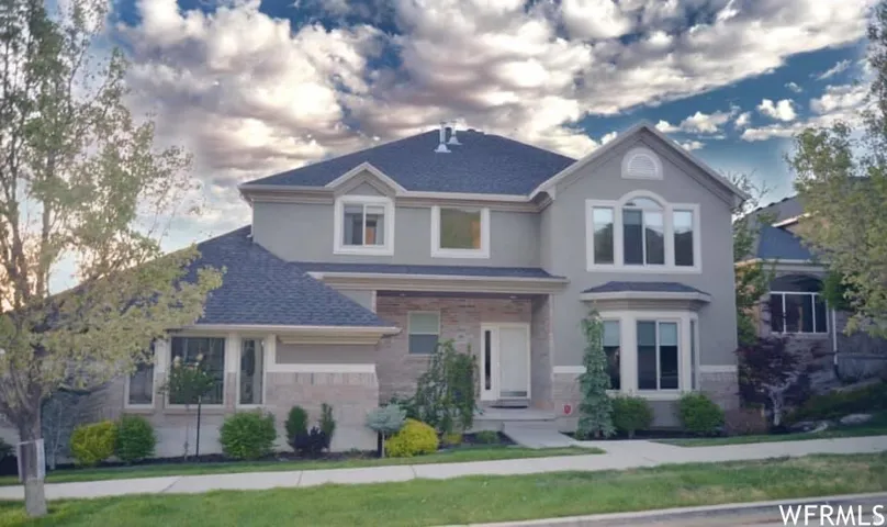 Multi-level exterior with a light-colored stucco finish, stone detailing, and a dark shingle roof