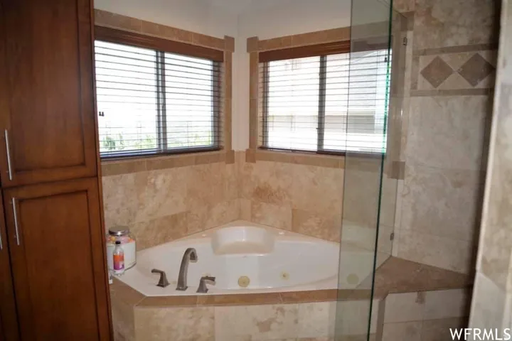 Corner soaking tub with deck-mounted faucet, tile surround, and adjacent glass-enclosed shower