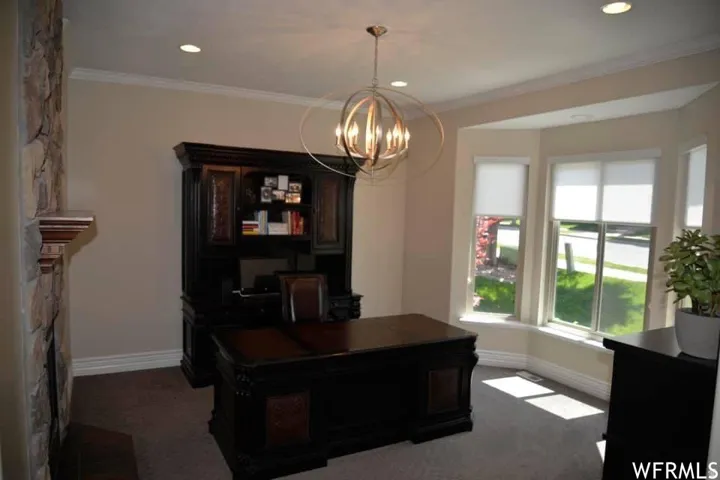 Stone-clad fireplace with mantel, bay windows, crown molding, recessed lighting, and a contemporary chandelier