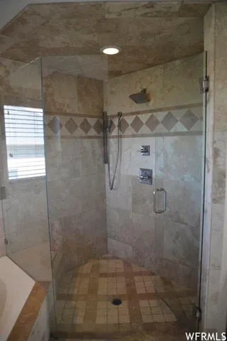 Tiled shower enclosure with a glass door, wall-mounted showerhead, handheld shower fixture, and recessed lighting