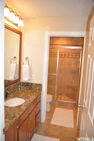 Bathroom featuring an extended vanity with a built-in sink, stone countertop, wood-finish cabinetry, and a walk-in shower with a glass enclosure and built-in bench