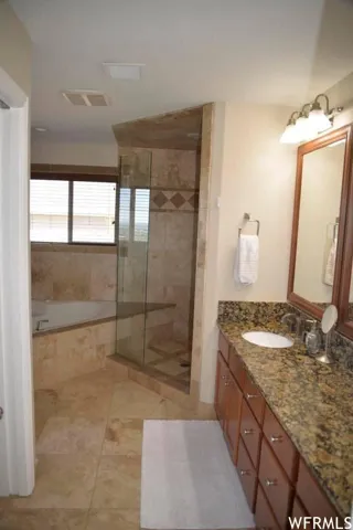 Built-in corner soaking tub, glass-enclosed shower with tiled surround, wood-finish vanity with stone countertop, and an integrated basin