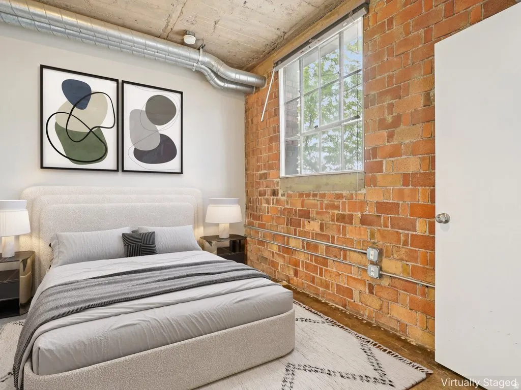 Exposed brick wall, large industrial window, concrete ceiling, exposed ductwork, and wood-finish flooring