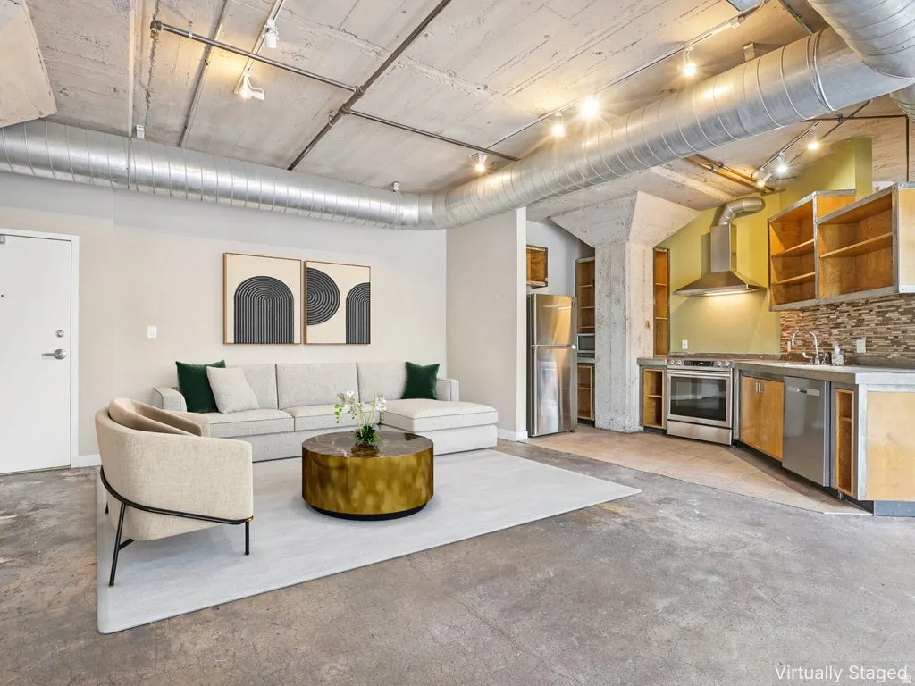 Exposed concrete ceiling with track lighting, visible ductwork, concrete flooring, stainless steel range hood, and tile backsplash