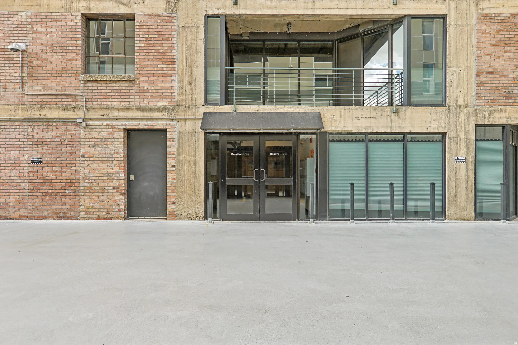 Brick and concrete facade with multiple window styles, a glass-paneled entrance, and a second-level balcony with metal railing
