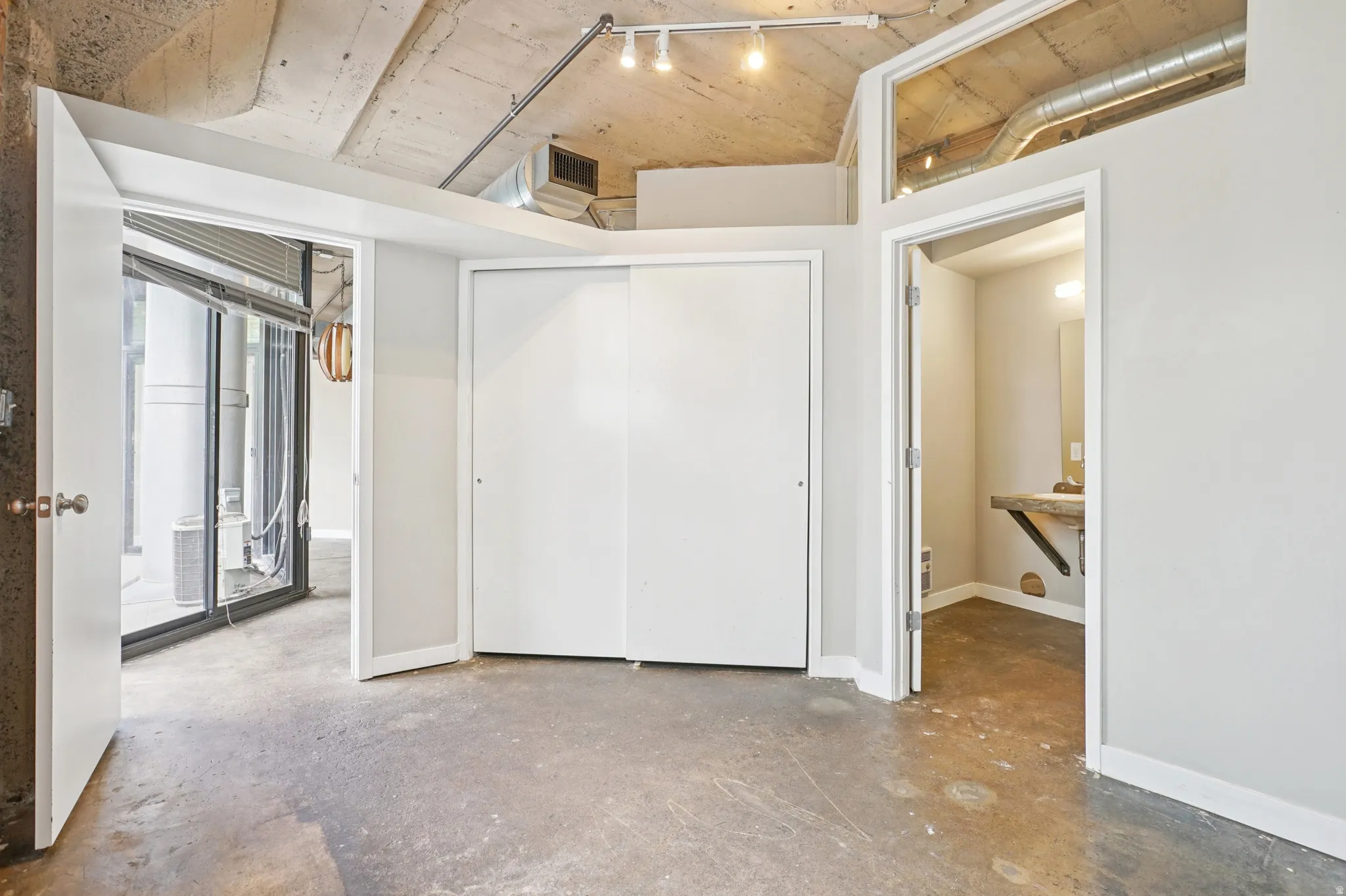 Concrete flooring, exposed concrete ceiling, sliding closet doors, track lighting, and a separate room with a vanity