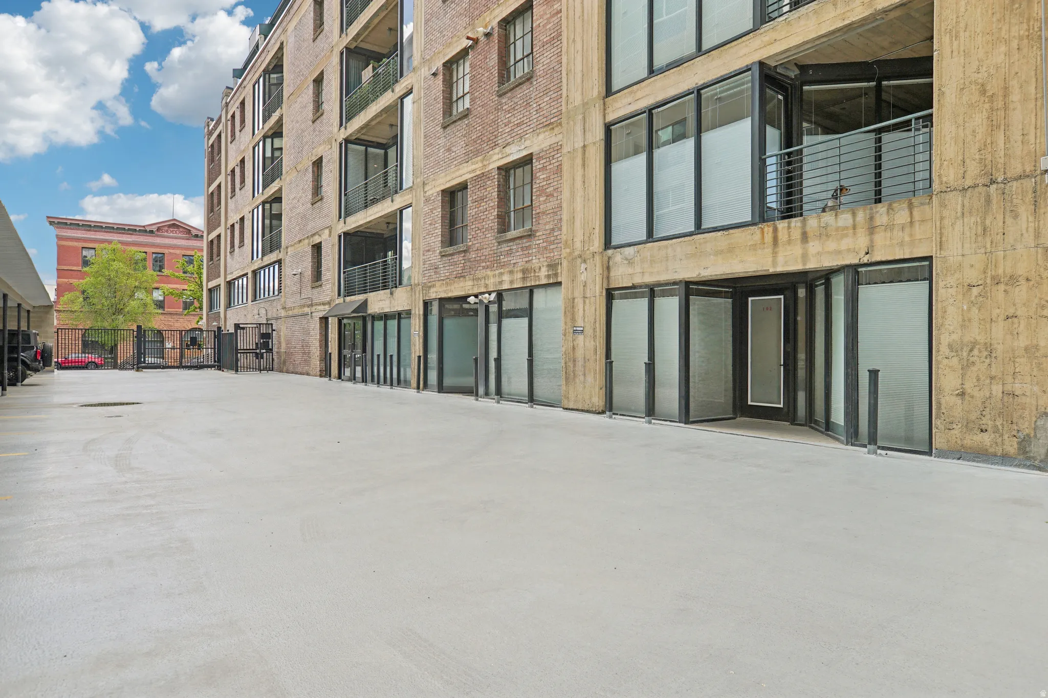 Concrete paving, brick and concrete building facade, multi-level balconies with metal railings, and ground-level glass storefronts