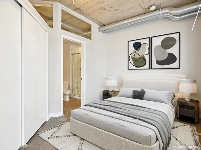 Exposed concrete ceiling with visible ductwork, concrete flooring, sliding closet doors, and an en-suite bathroom with a glass-enclosed shower