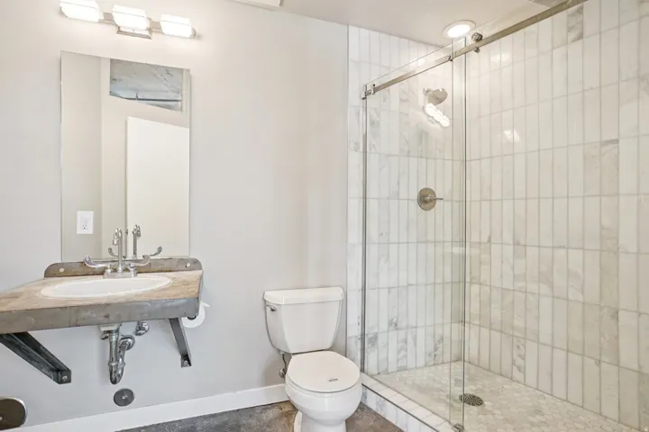 Walk-in shower with vertical tile surround and hexagonal tile floor, glass shower door, and brushed nickel hardware
