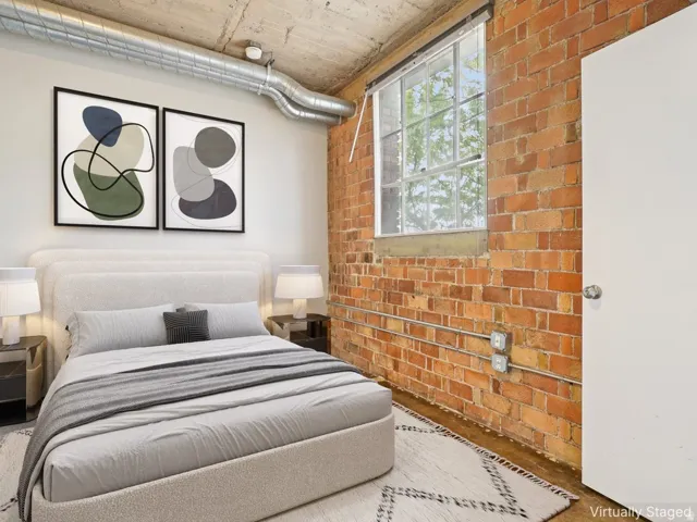 Exposed brick wall, large industrial window, concrete ceiling, exposed ductwork, and wood-finish flooring