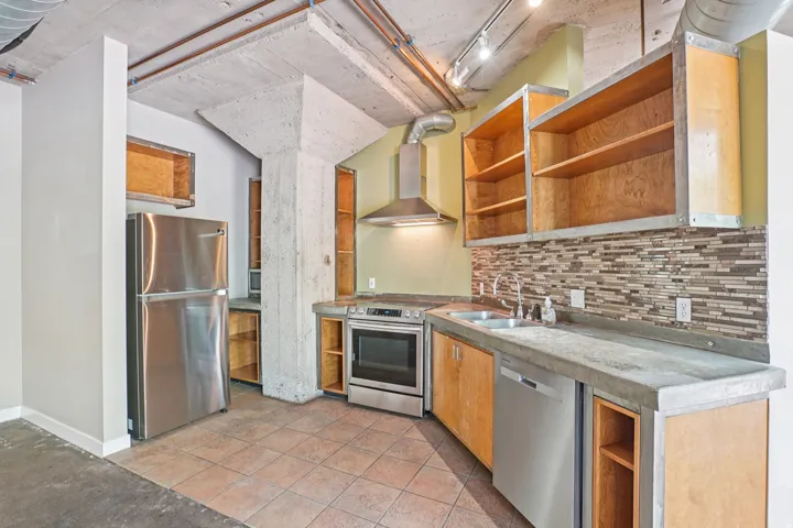Kitchen featuring tile flooring, concrete countertops, stainless steel appliances, and a mosaic tile backsplash