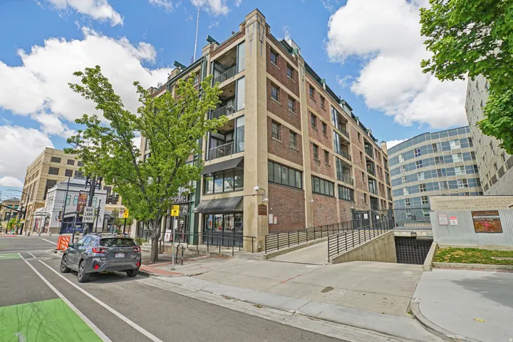 Brick exterior with multiple balconies, ground-level retail spaces, and a concrete ramp to an underground garage