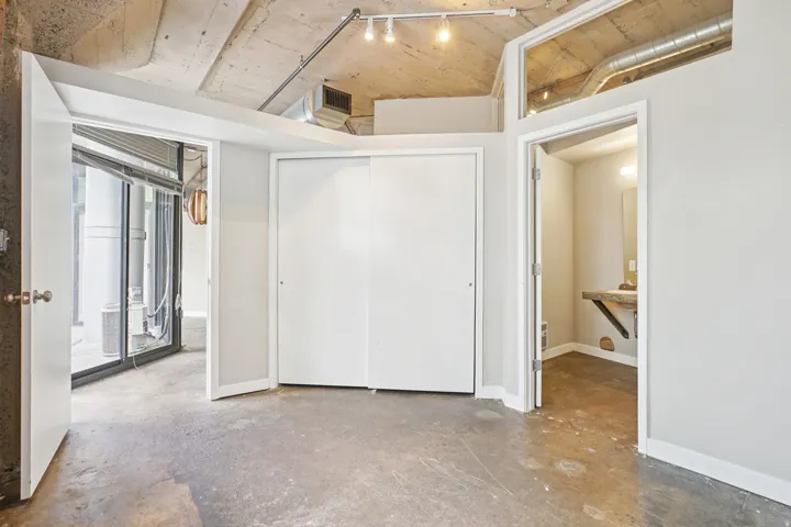 Concrete flooring, exposed concrete ceiling, sliding closet doors, track lighting, and a separate room with a vanity