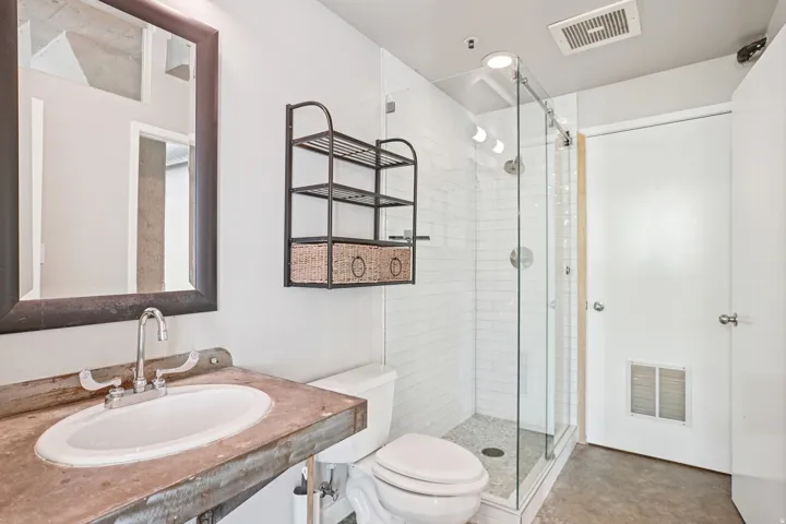 Walk-in shower with clear glass enclosure and subway tile surround, vanity with an integrated sink and metal countertop, wall-mounted mirror with dark frame, and recessed lighting