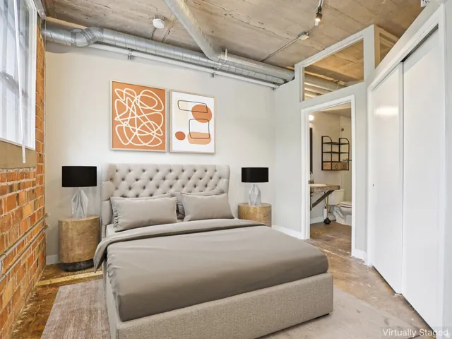 Exposed brick accent wall, concrete ceiling with visible ductwork, track lighting, sliding closet doors, and wood-finish flooring