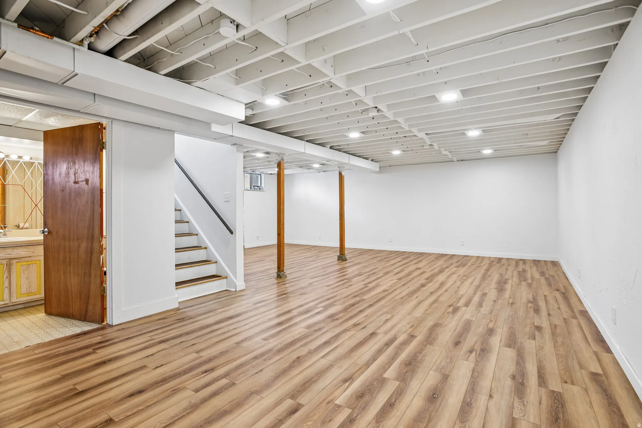 Expansive finished lower level featuring wood-finish flooring, recessed lighting, white painted walls, and an exposed joist ceiling