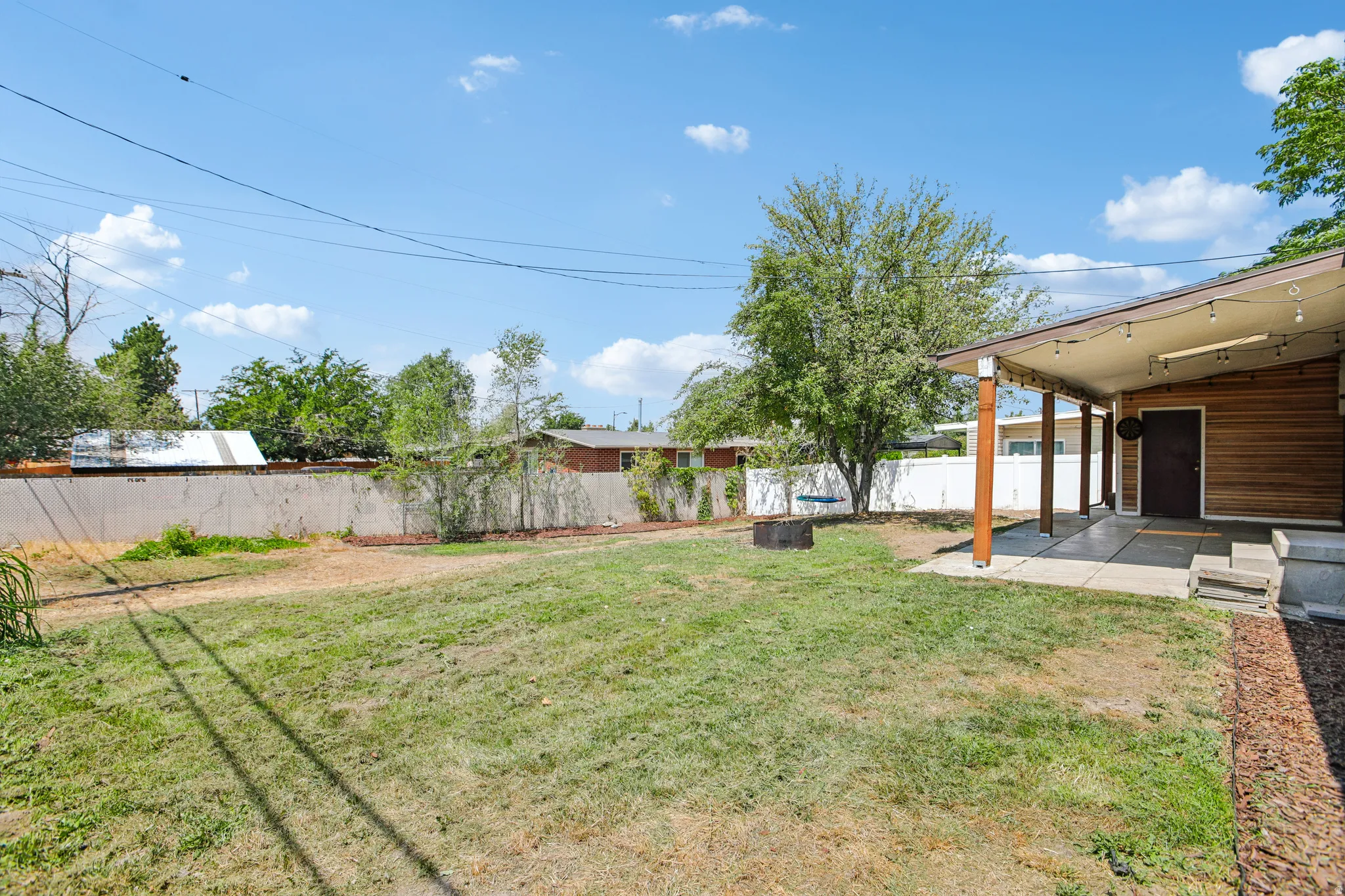 Expansive backyard featuring a covered patio, concrete surface, wood-paneled exterior, and a fire pit