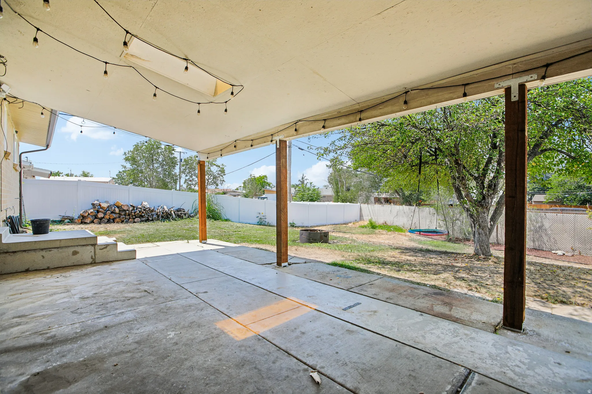 Expansive covered patio with concrete flooring, supported by wood posts, overlooking a grass yard with a fire pit