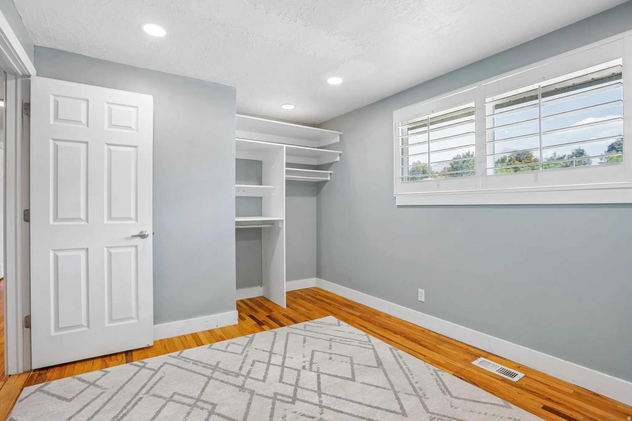 Hardwood flooring, recessed lighting, built-in closet shelving, window with plantation shutters, and a six-panel door