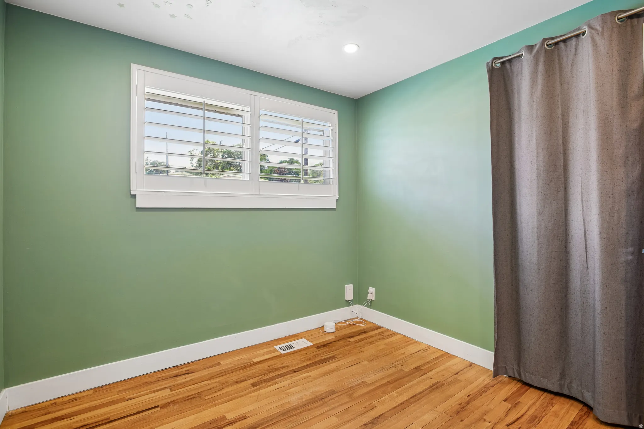 Hardwood flooring, recessed ceiling lighting, window with plantation shutters, and a curtain rod