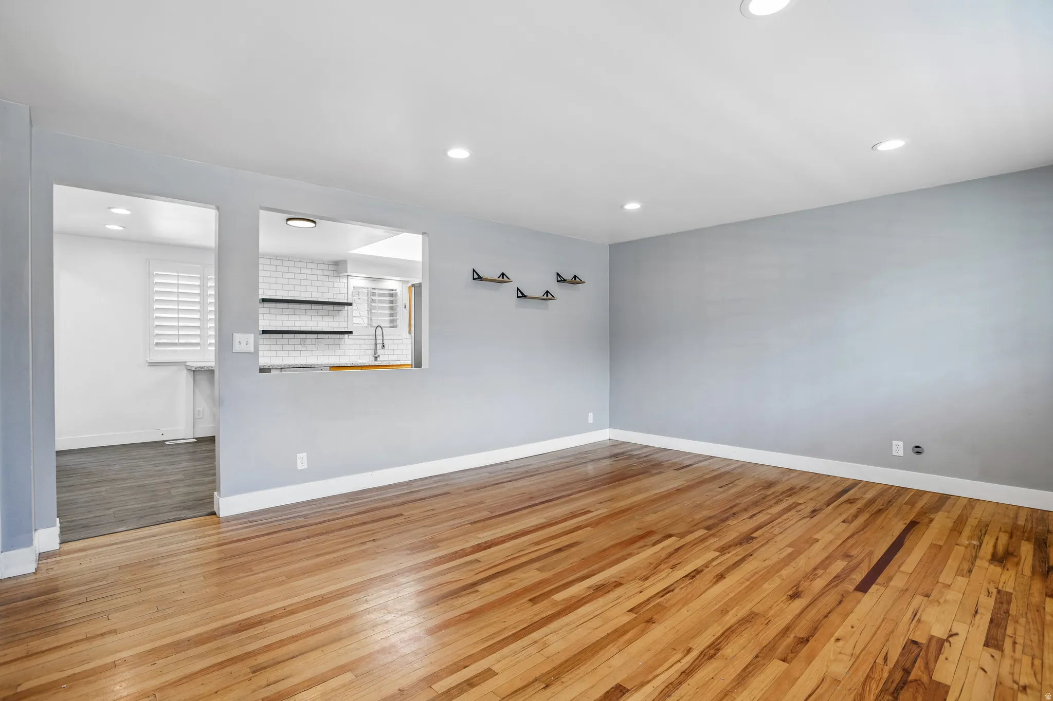 Hardwood flooring throughout, recessed lighting, and a pass-through opening to the kitchen featuring subway tile backsplash and open shelving