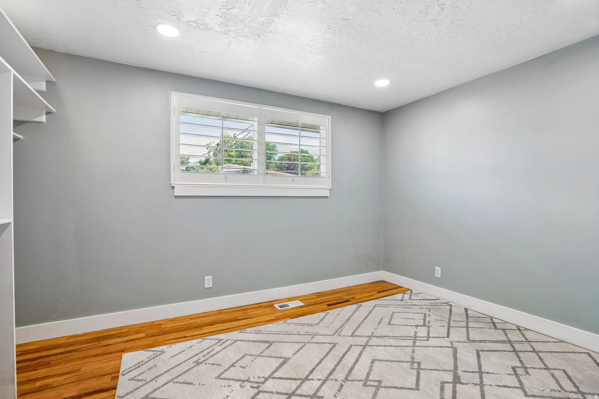 Recessed lighting, wood-finish flooring, white plantation shutters, built-in shelving, and white baseboards