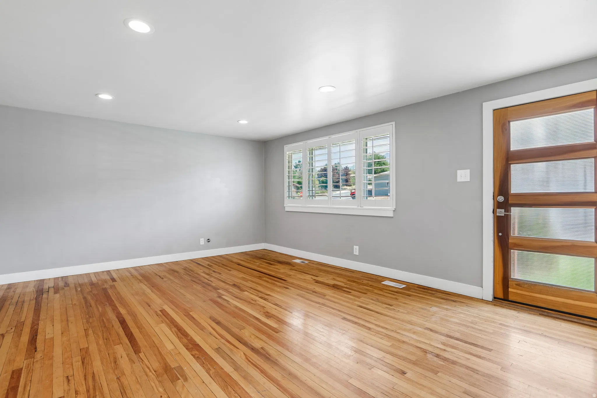 Hardwood flooring, recessed lighting, modern entry door with frosted glass panels, window with white plantation shutters, and light gray wall paint