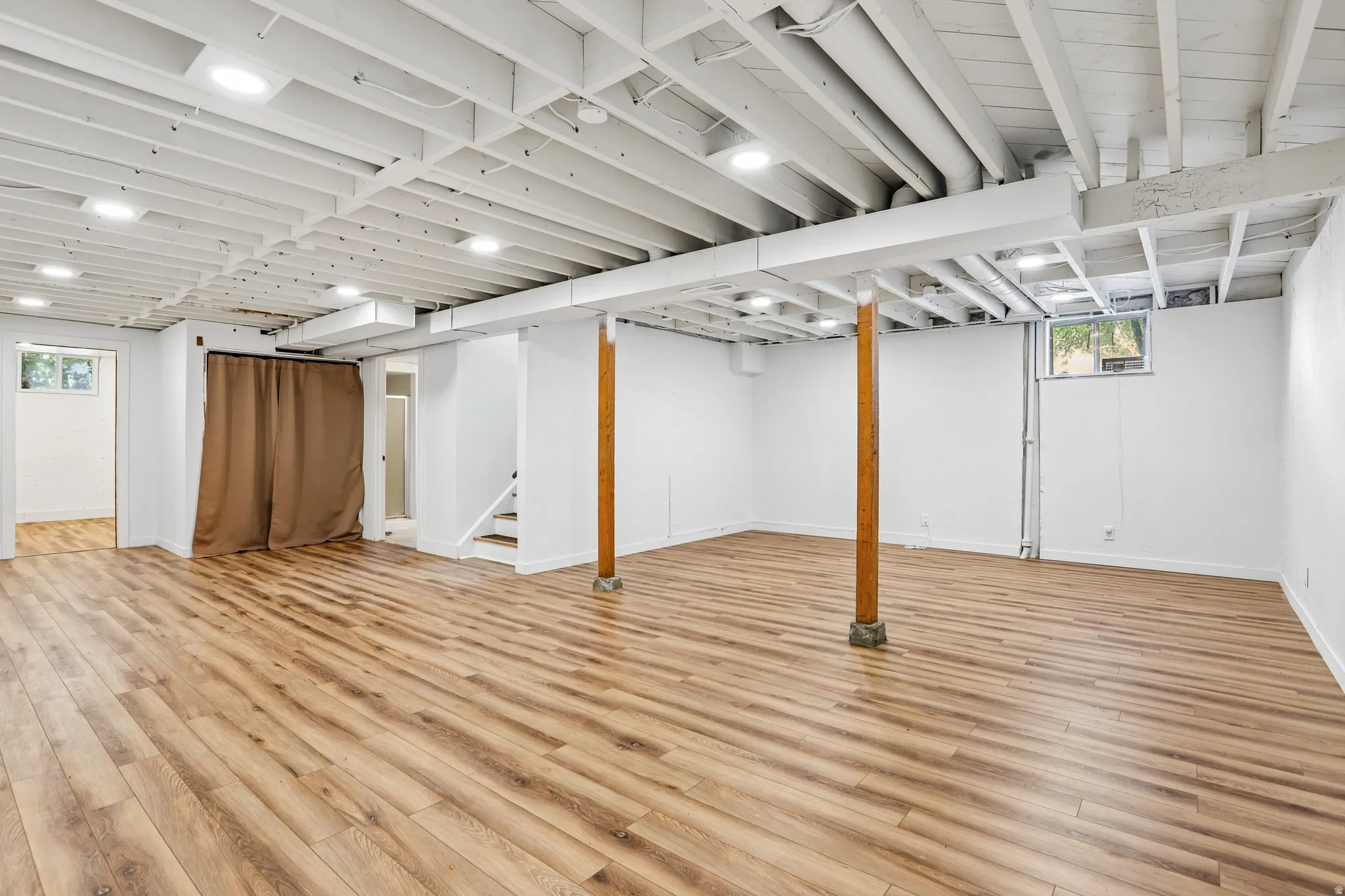 Expansive space featuring wood-finish flooring, recessed lighting, white walls, and exposed white ceiling joists