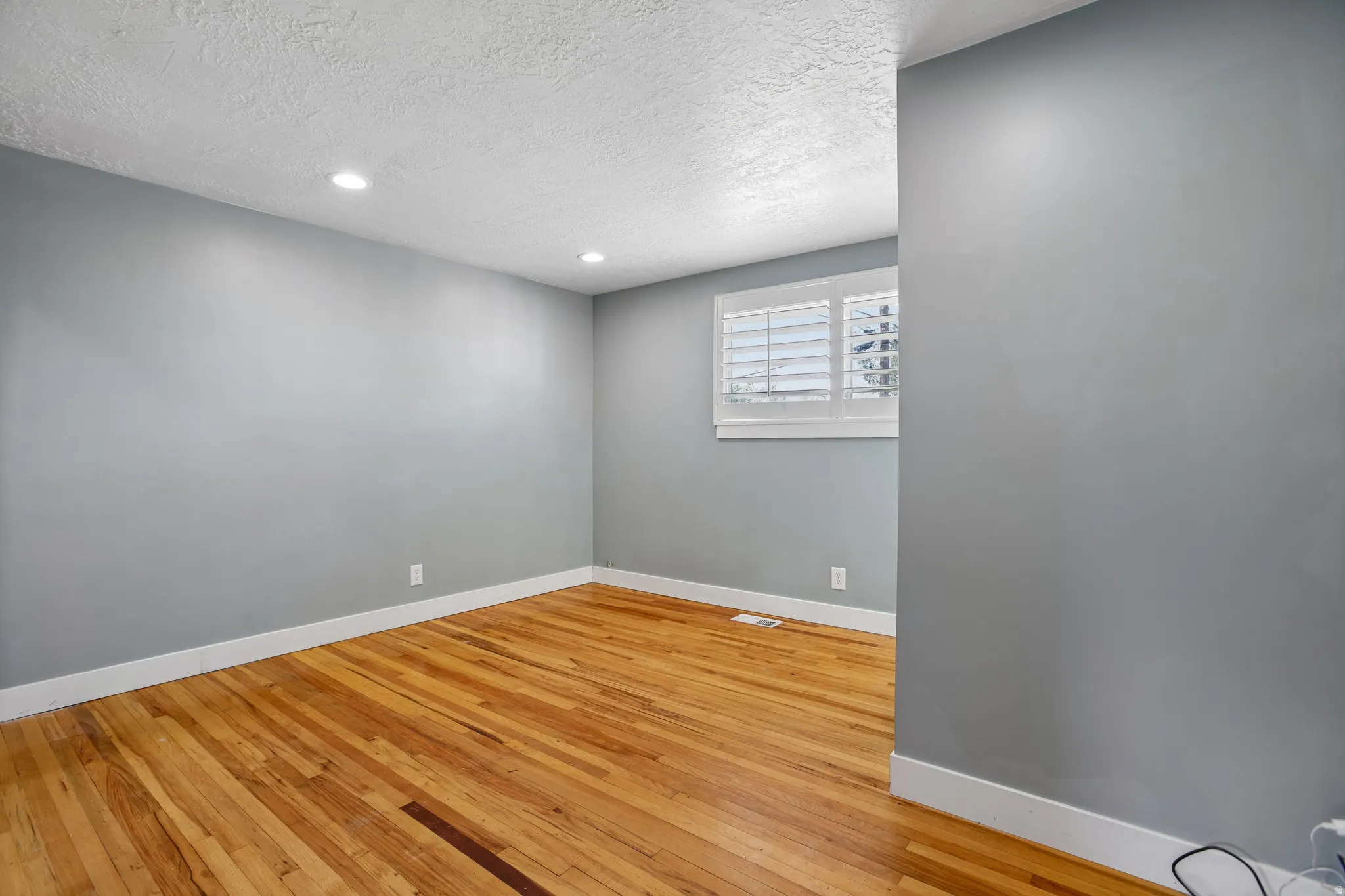 Hardwood flooring, recessed lighting, window with plantation shutters, light-toned walls, and white trim