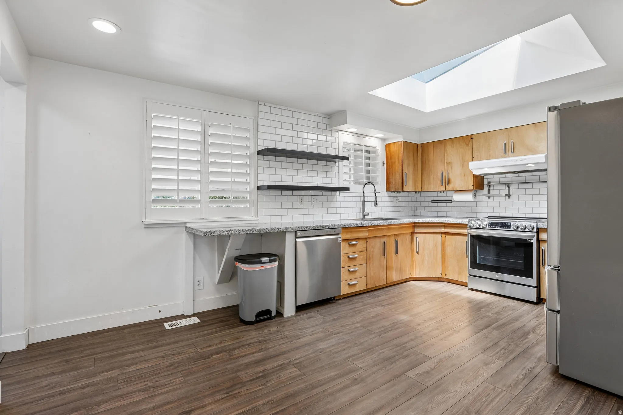 Kitchen featuring wood-finish flooring, wood cabinetry, granite countertops, white subway tile backsplash, and a skylight