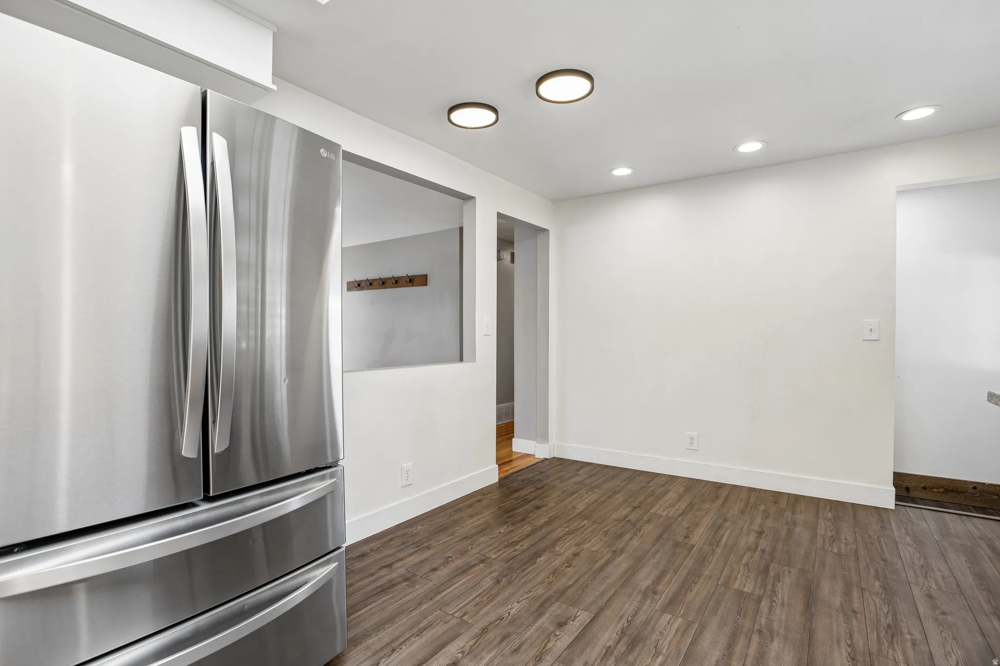 Stainless steel French door refrigerator, wood-finish flooring, recessed lighting, and a pass-through opening