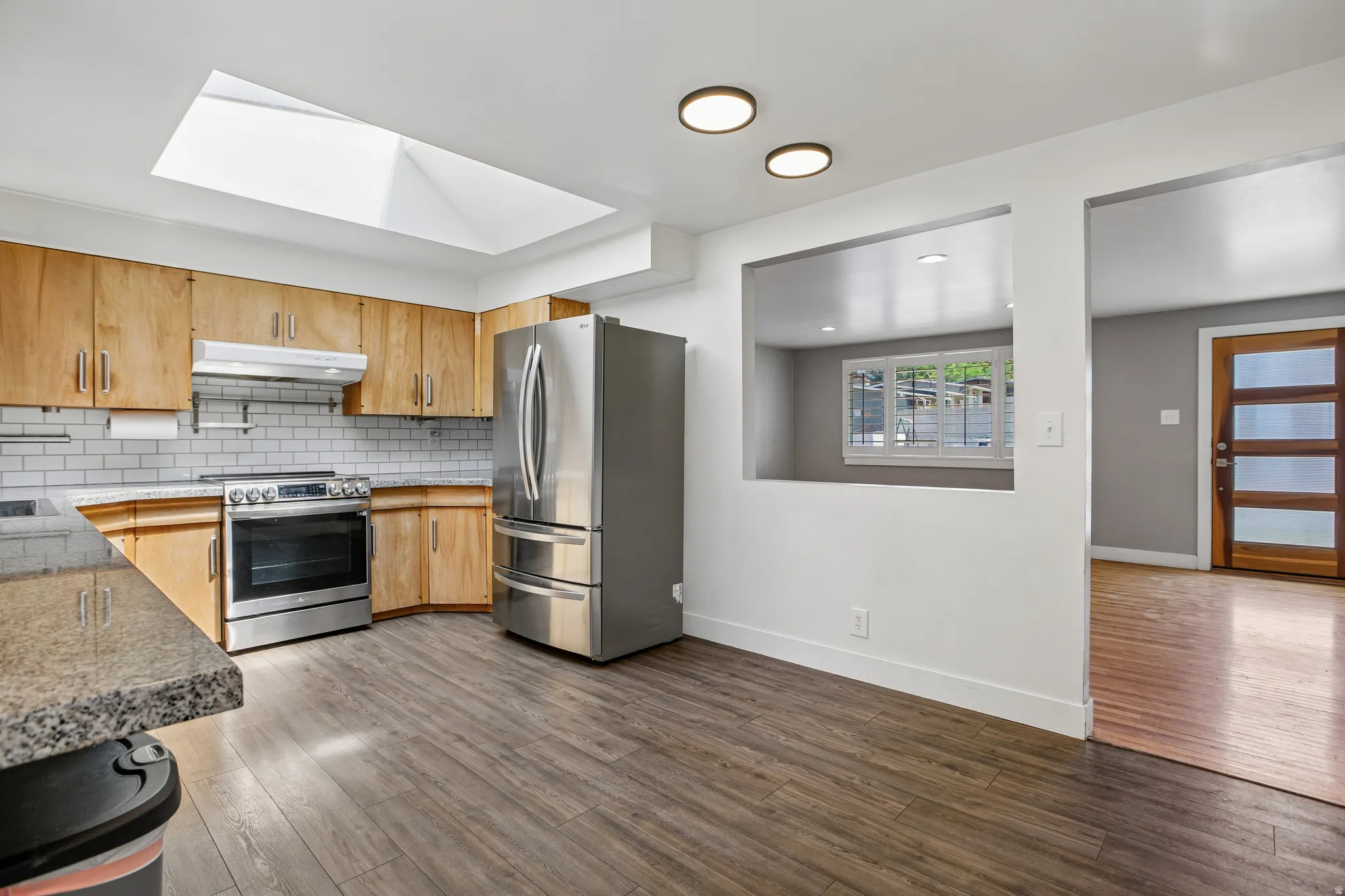 Kitchen featuring a skylight, wood-finish cabinetry, stainless steel appliances, granite-look countertops, and wood-finish flooring