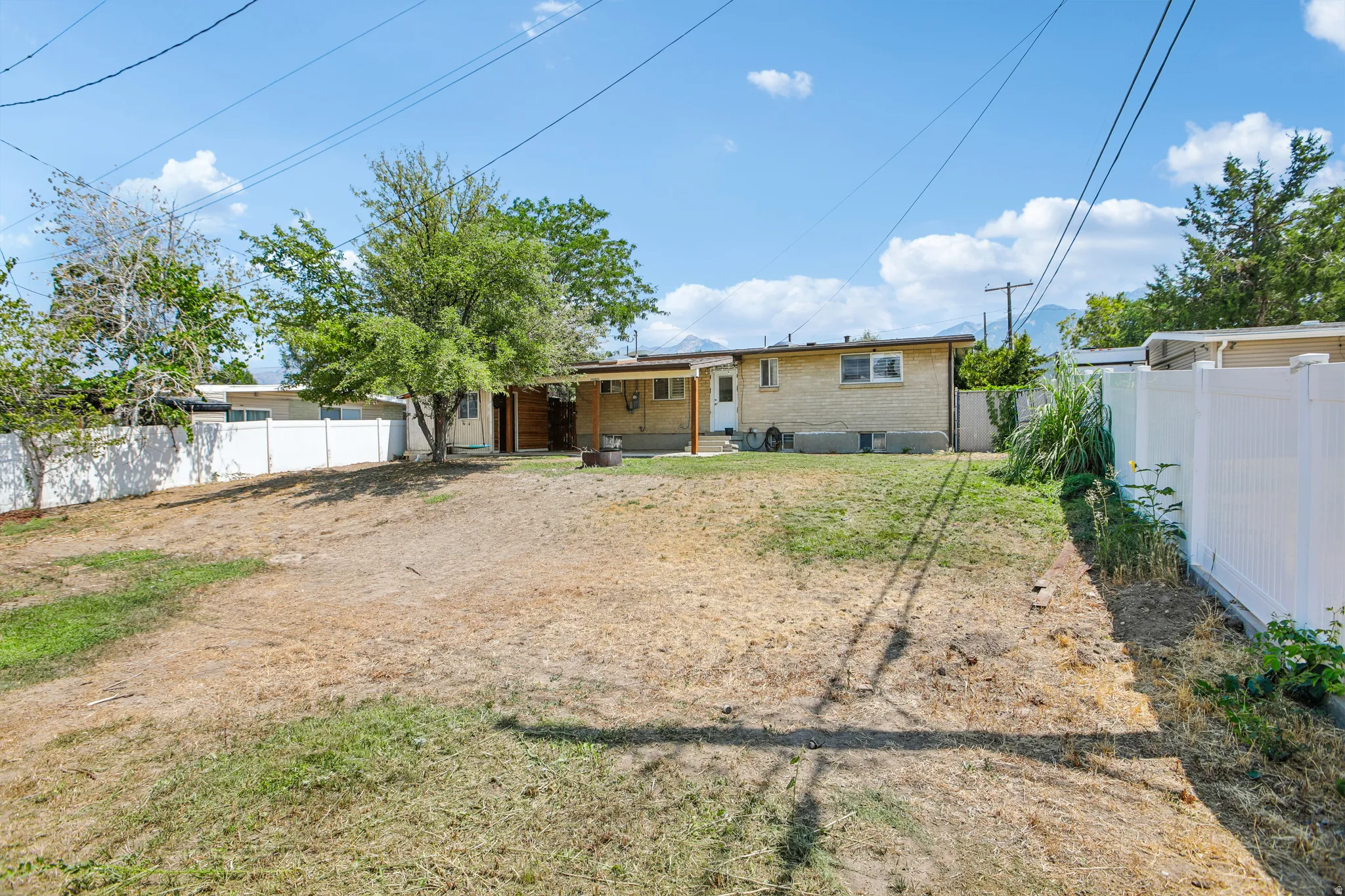 Expansive backyard featuring a partial vinyl fence, mature trees, and an exterior patio with a covered awning