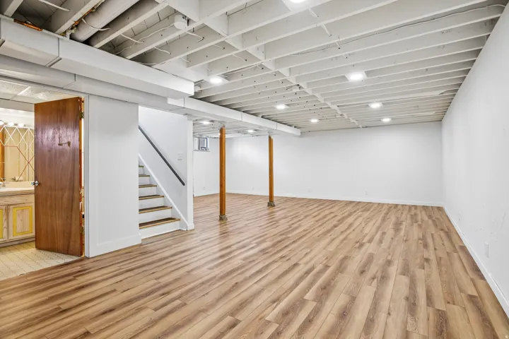 Expansive finished lower level featuring wood-finish flooring, recessed lighting, white painted walls, and an exposed joist ceiling