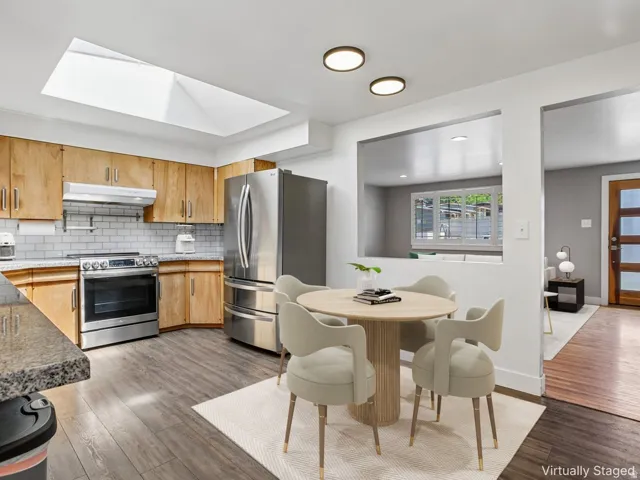 Open-concept kitchen and dining area featuring stainless steel appliances, wood-finish cabinetry, subway tile backsplash, wood-finish flooring, and a skylight above
