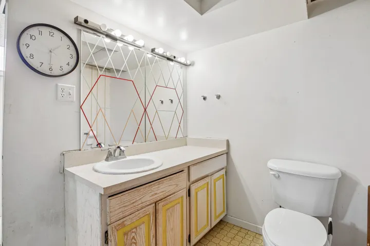 Single basin vanity with cabinet storage, mounted mirror with integrated lighting, and a white toilet