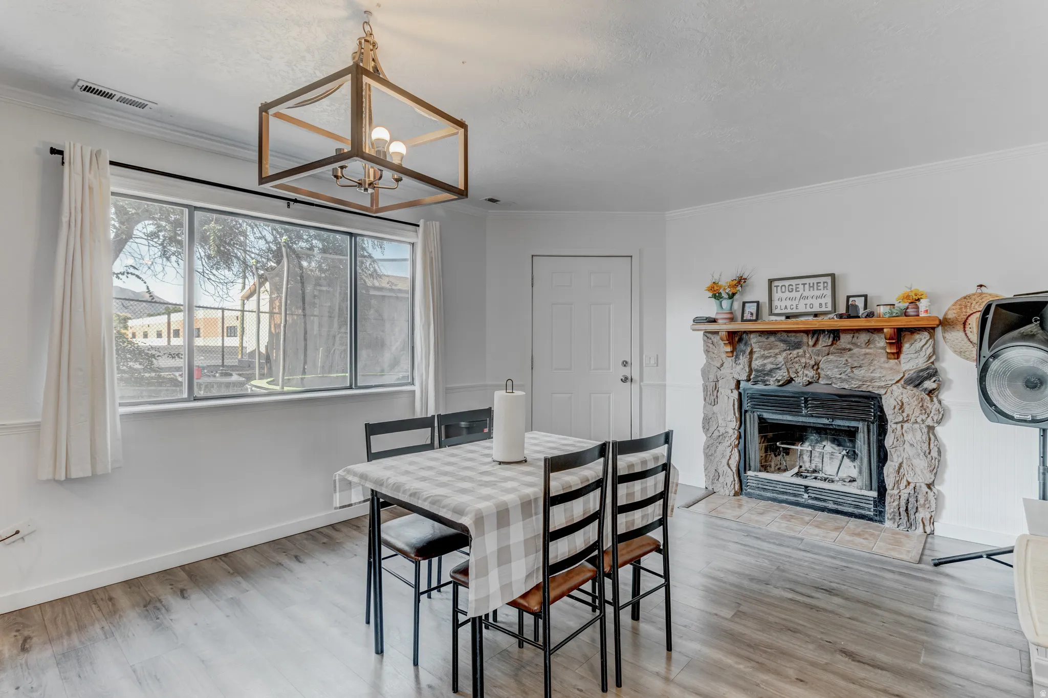 Wood-finish flooring, a stone fireplace with a wood mantle, and a contemporary cage-style chandelier