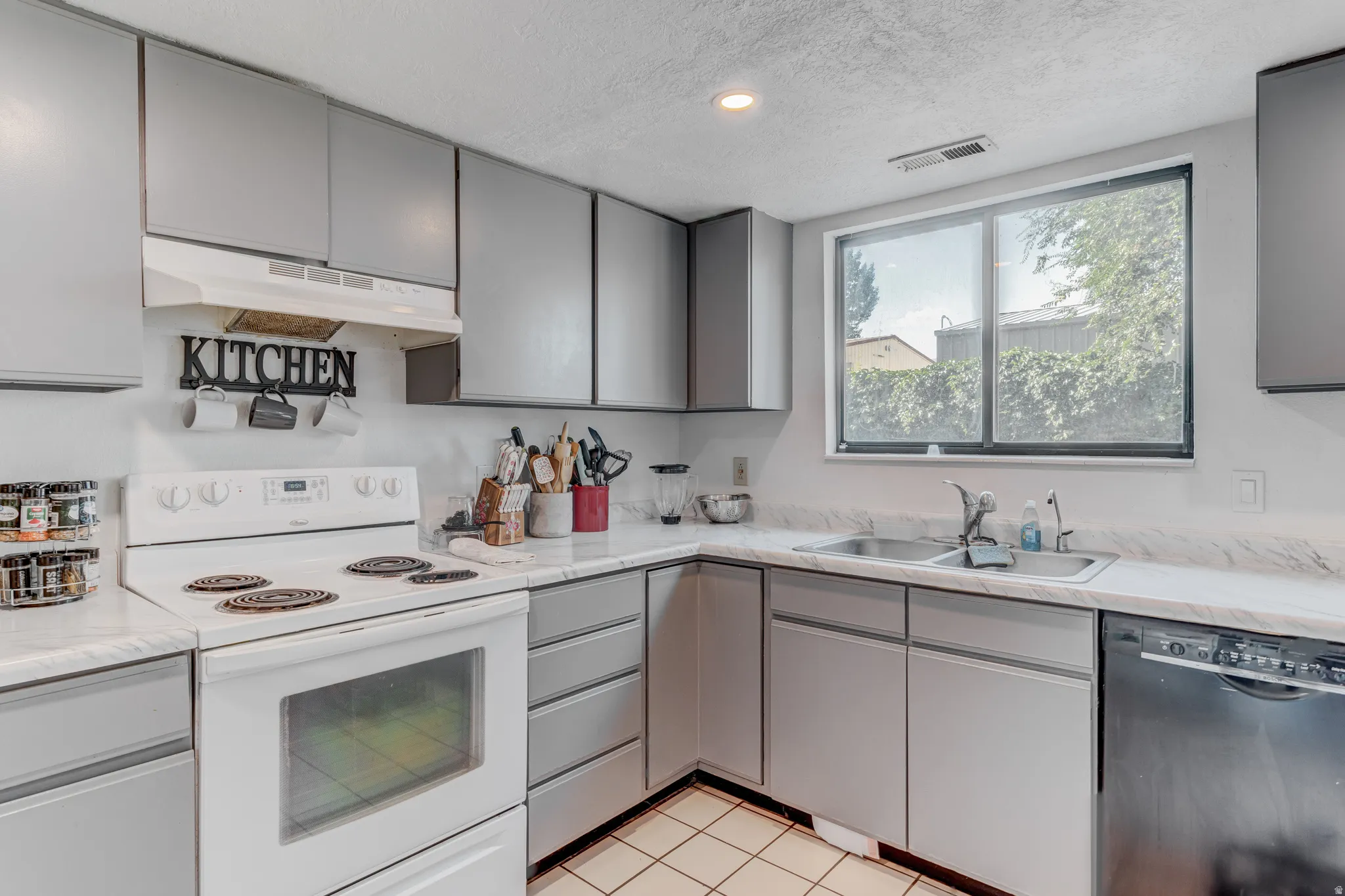 Full kitchen featuring gray cabinetry, white countertops, white range, stainless steel double basin sink, and a black dishwasher