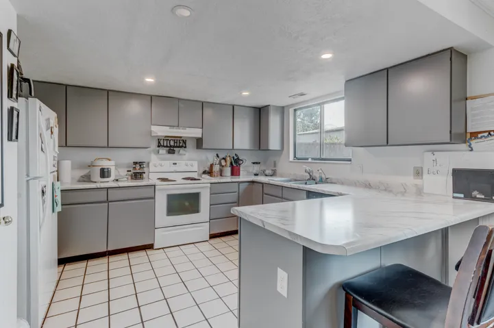 U-shaped kitchen featuring grey cabinetry, white tile flooring, white appliances, and light-toned countertops