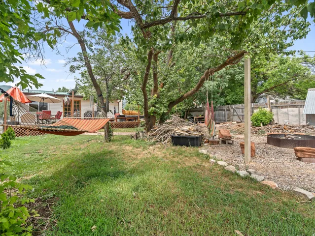 Expansive backyard featuring a manicured lawn, established shade trees, and a gravel-covered entertainment area with a fire pit