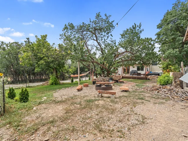 Expansive outdoor space featuring a fire pit, mature trees, a wood deck, and a fenced perimeter