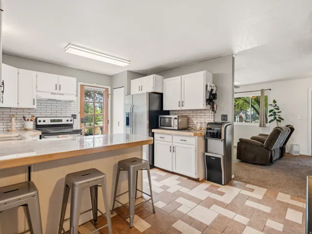 Kitchen with white cabinetry, tile backsplash, wood-finish countertops, and patterned tile flooring